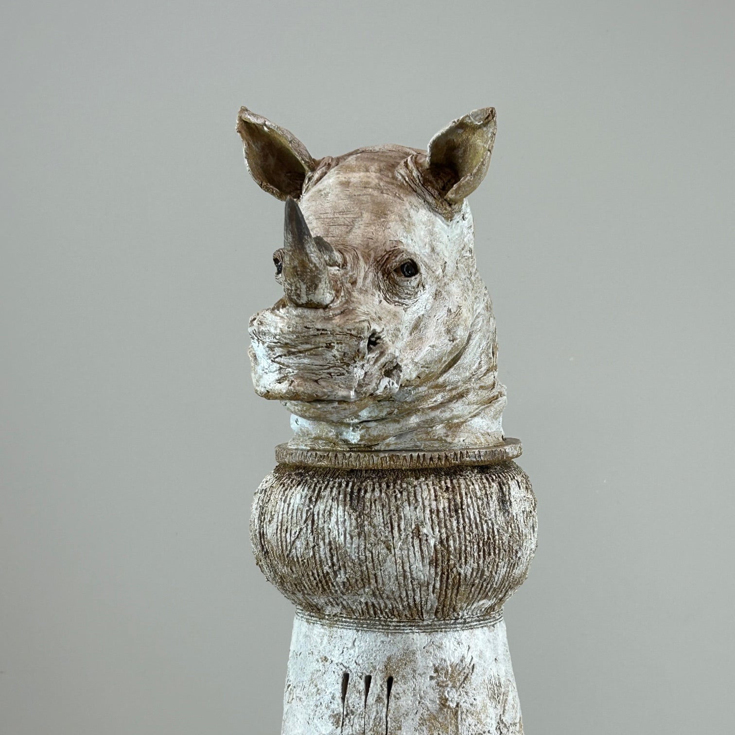 Statue of a rhinoceros head on a pedestal against a gray background